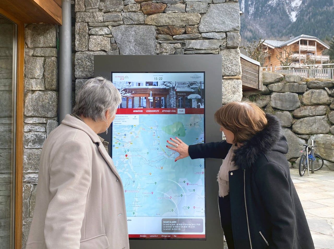 Deux passantes consultant une borne d'affichage légal extérieure
